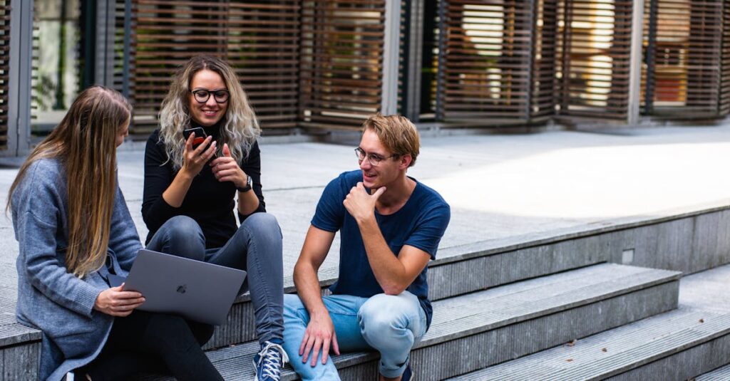 Contact Three young professionals having a friendly chat while sitting on outdoor steps.