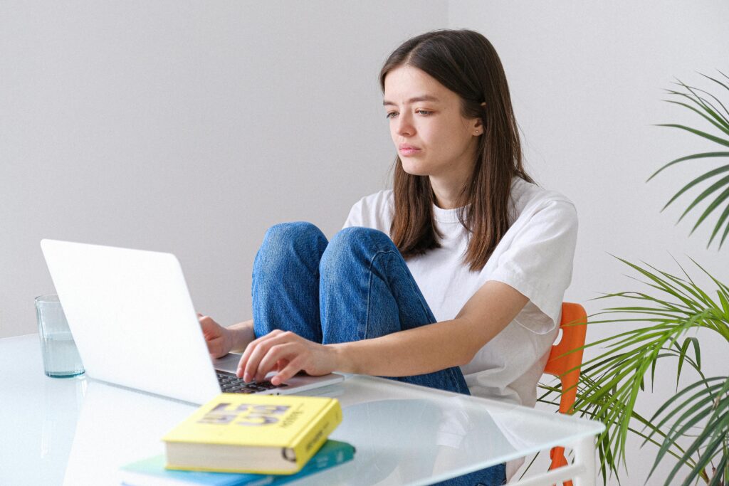 Young woman in blue jeans working on laptop from home office, embracing remote work lifestyle.