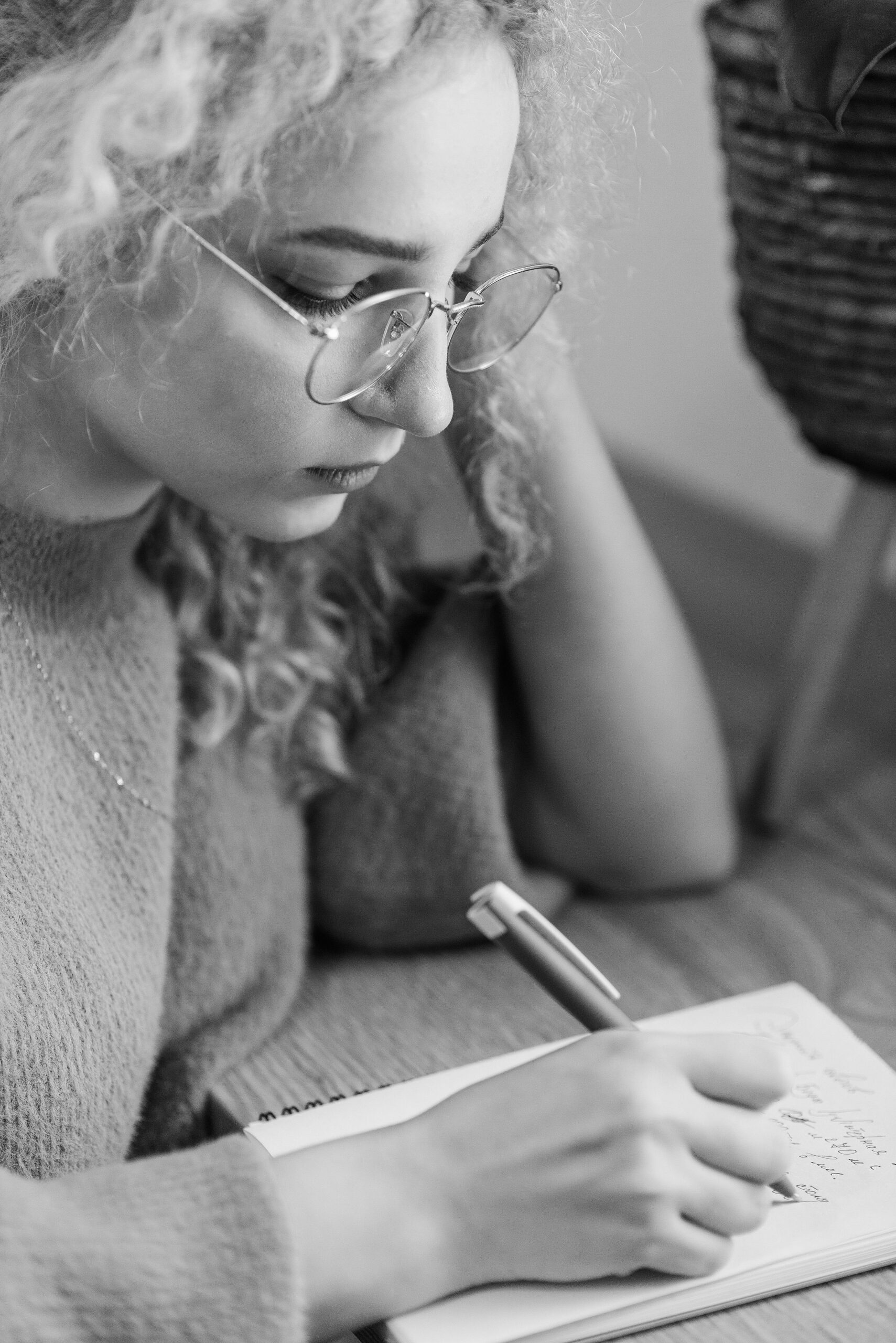Caucasian woman with eyeglasses writing in a notebook, captured in black and white.